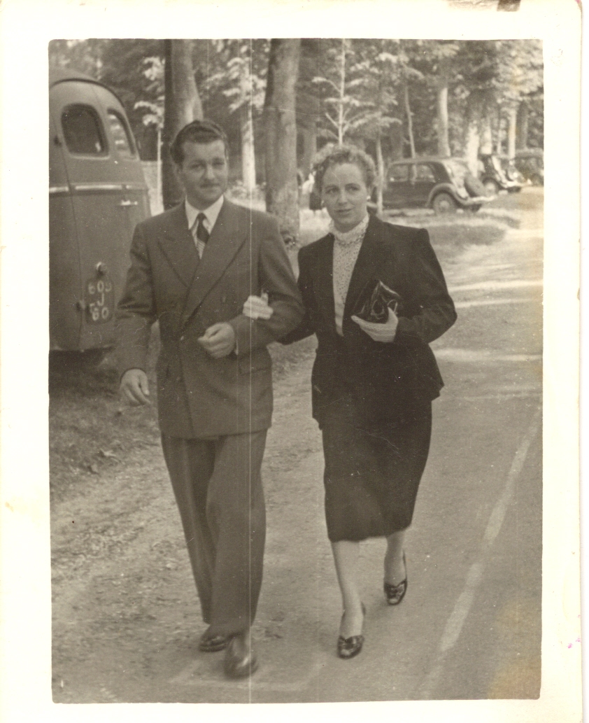 photographie en noir et blanc d'un couple élégant marchant dans la rue avec voiture années 1950